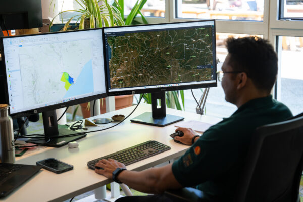 Shanyal Uqaili arbeitet an zwei Bildschirmen mit Satellitenkarten und Geodaten zur Analyse von Schutzgebieten.